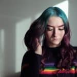HappyMapz. Young woman with colorful hair looking down, indoor portrait, vibrant hair, expressive mood.